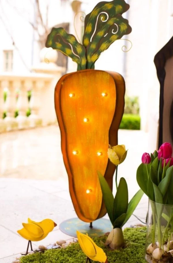 Osterdeko draußen übergroße Karotte mit kleinen Leuchten Küken Tulpen