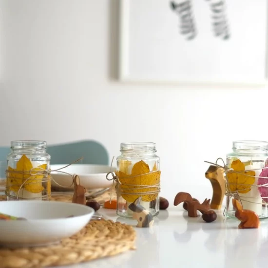 Esszimmer herbstlich dekorieren Esstisch schmücken kleine Holzfiguren neben Einmachgläsern mit gelben Blättern arrangiert
