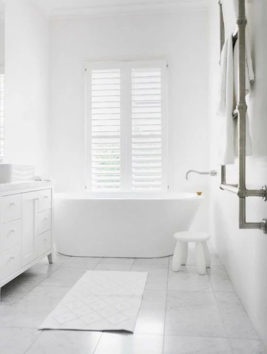 Badezimmer ganz in Weiß Badewanne vor dem Fenster Sichtschutz viel natürliches Licht kleiner Hocker