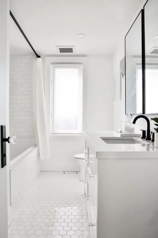 Badezimmer ganz in Weiß weiße Metro Fliesen an der Wand andere Form auf dem Boden schwarze Armaturen Fenster viel natürliches Licht