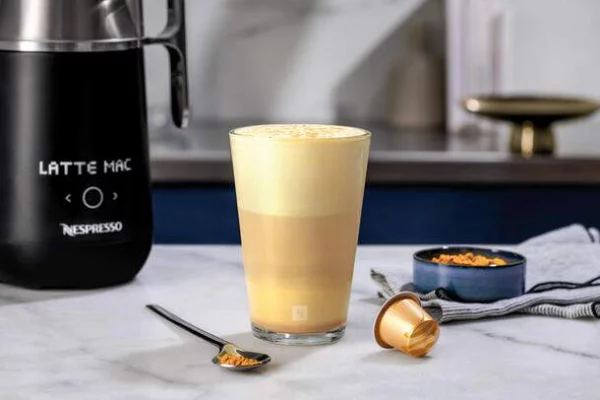Kurkuma Kaffee in Schichten mit viel Schaum darauf Espresso Kanne daneben
