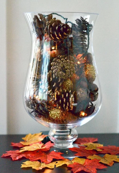 Herbstdeko mit Tannenzapfen ein hohes Glas mit gefärbten Zapfen mit Goldglanz verziert Blickfang