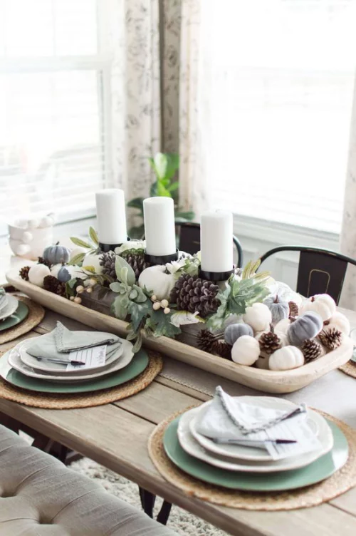 Herbstdeko mit Tannenzapfen weiße Kerzen Zapfen Blätter in einer Holzschale in der Tischmitte festlich gedeckter Tisch