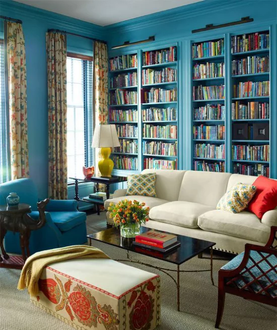 Eingebaute Bücherregale Wohnzimmer klassisches Raumdesign Blau dominiert Sessel helles Sofa Hocker Lampe gelbe Gardinen