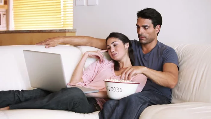 Keine langfristige Beziehung Sternzeichen ein junges Paar verliebt auf der Couch zuhause Laptop zufrieden ausgeglichen