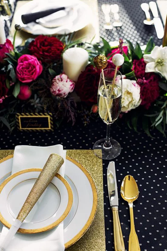 Silvester feiern zu Hause stilvolles Tischarrangement Schwarz Weiß Gold dunkelrote Blüten in der Mitte
