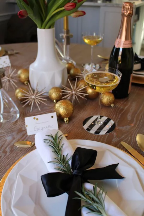 Silvester feiern zu Hause weiße Serviette schwarzes Band viele Goldglitzer Sektflasche Vase mit Tulpen