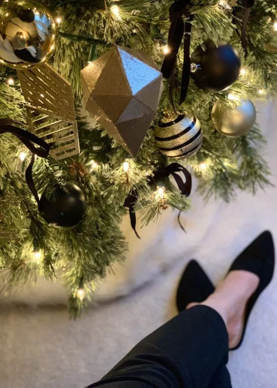 Weihnachtsdeko in Gold und Schwarz Christbaum goldgelbe und schwarze Kugeln weitere Ornamente Schleifen eine Frau daneben