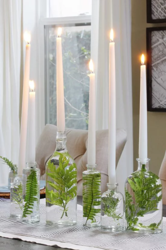 skandinavische Frühlingsdeko Glasvasen mit grünen Blättern darin brennende weiße Kerzen sehr elegantes Arrangement