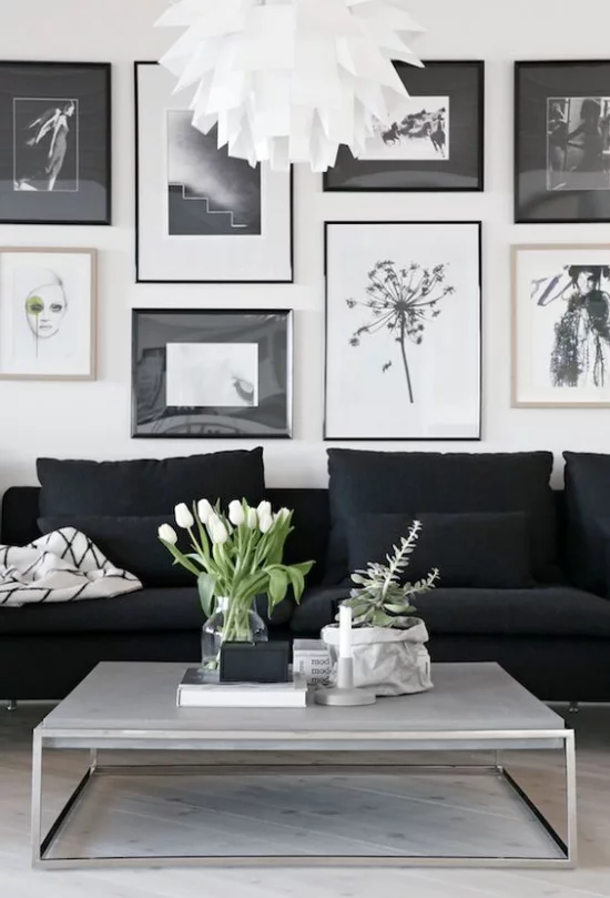 skandinavische Frühlingsdeko schönes Wohnzimmer elegante Möbel Wandbilder schwarze Couch niedriger Tisch weiße Tulpen