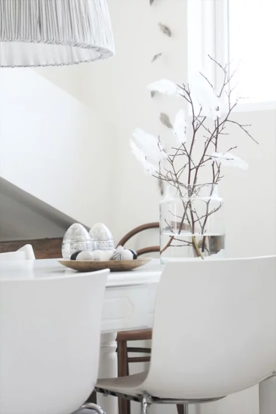 skandinavische Frühlingsdeko weißes Ambiente auf dem Tisch interessantes Arrangement Glasvase Zweige Federn Eier