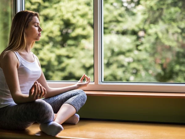 Relaxed woman in Lotus position by the window.