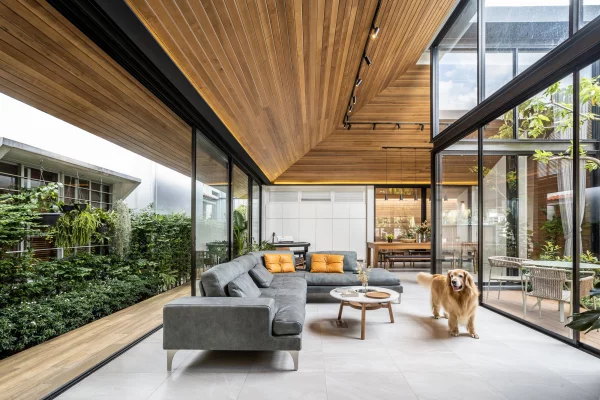Open-Air-Wohnzimmer vertikaler Garten links bequeme Sitzmöbel deckenhohe Glaswände Hund großzügiges Raumkonzept
