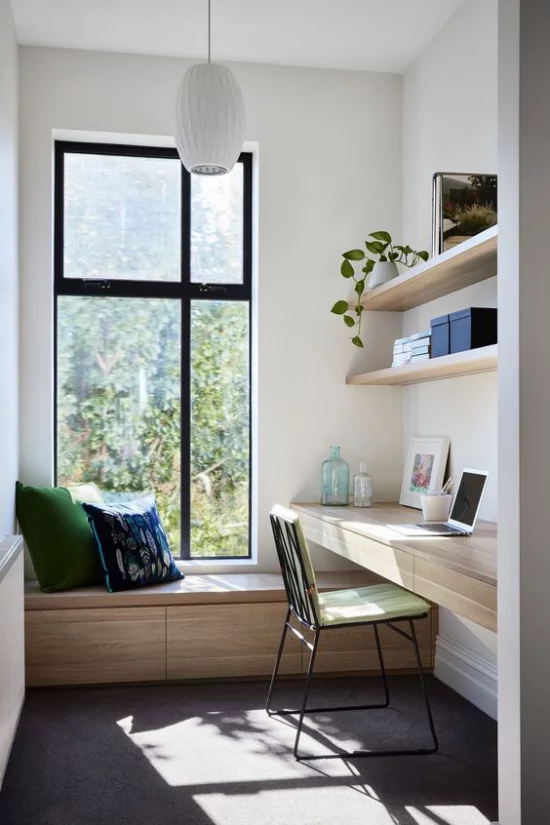zeitgenössisches Home Office einfach aber gemütlich eingerichtet Sitzbank weiße Kissen am Fenster Schreibtisch offenes Regal helles Holz