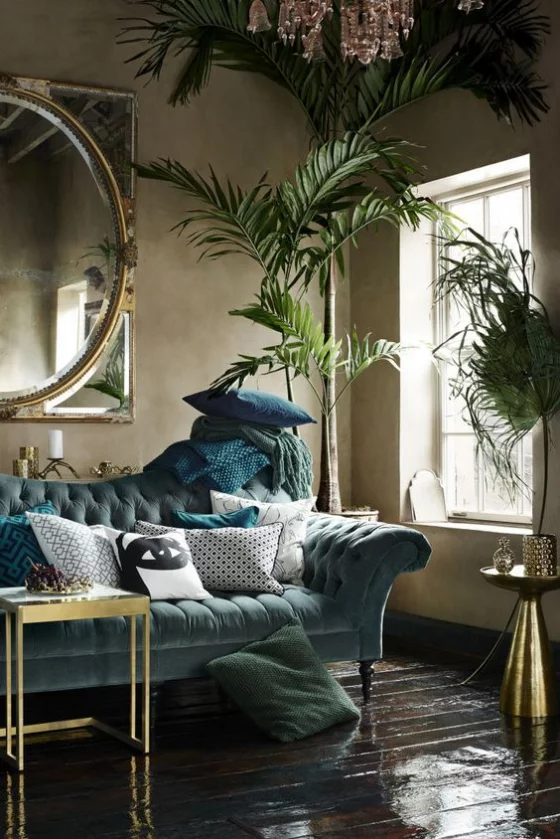 Goldene Akzente im Interieur dunkles Wohnzimmer etwas mysteriös viele Grünnuancen Couch Tisch runder Wandspiegel üppige Grünpflanzen