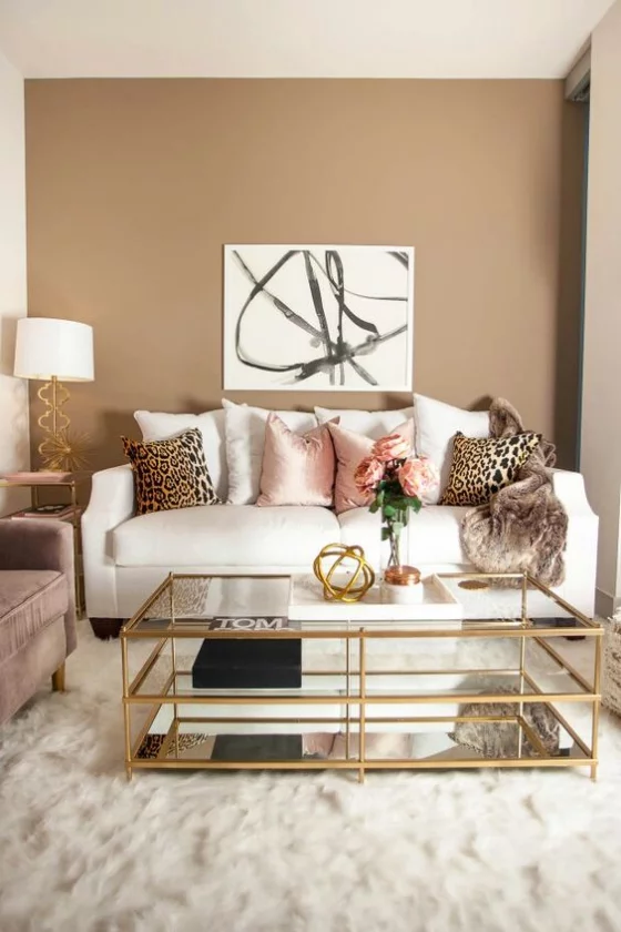 Goldene Akzente im Interieur gemütliches Wohnzimmer weiße Couch Tisch mit goldenen Kanten und Beinen weicher Teppich beigefarbene Wand
