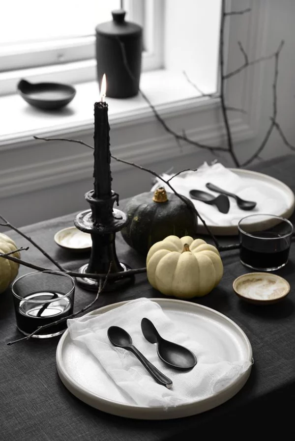minimalistische Halloween Deko Esstisch am 31.Oktober schwarzes Geschirr Besteck schwarze Tischdecke kahle Zweige schwarze Kerze