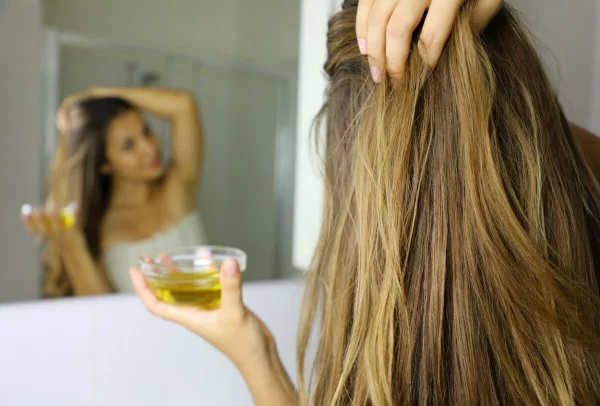 Oele für Haarwuchs junge Frau vor dem Spiegel Schuessel mit Oel aufs Haar auftragen