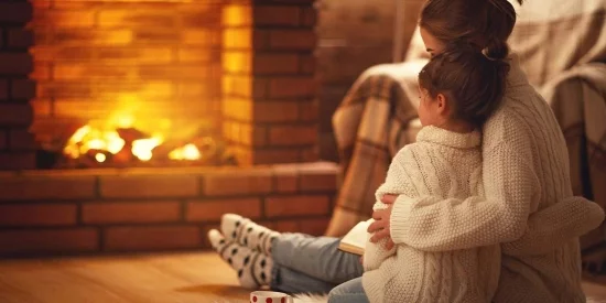Heizen mit Brennholz junge Mutter kleines Maedchen vor dem Kaminfeuer sitzen romantische Atmosphaere