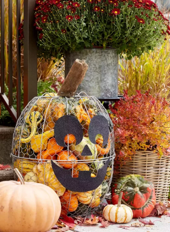 Herbstdeko draussen vor der Haustuer gruseliges Gesicht Metallgefaess voll mit kleinen Kuerbissen Halloween Deko