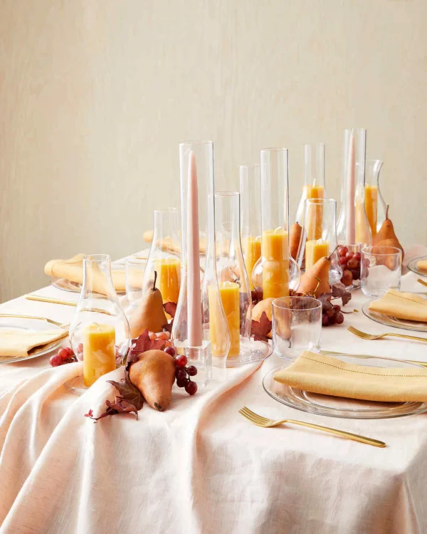 Herbstliche Tischdeko schoen gedeckter Tisch in der Titte viele orangefarbene Kerzen ind Glasgefaessen Birnen Trauben Blaetter
